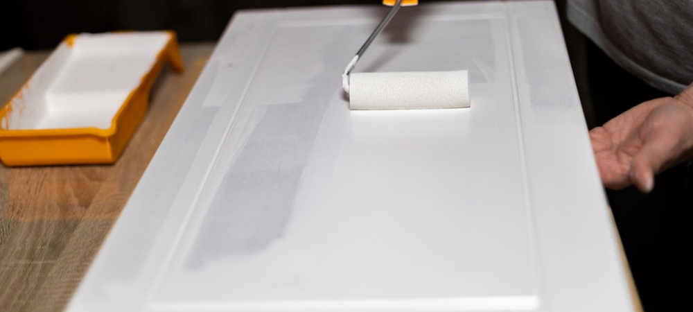 Applying fresh cabinet paint finish with roller brush