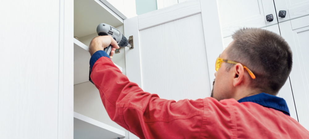 Worker using screwdriver to install kitchen cabinets
