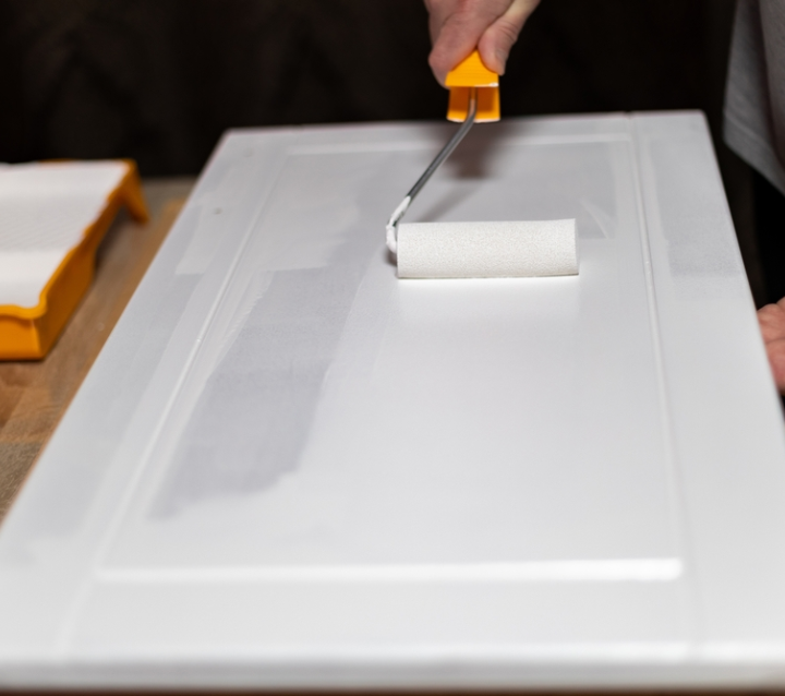 Applying fresh cabinet paint finish with roller brush