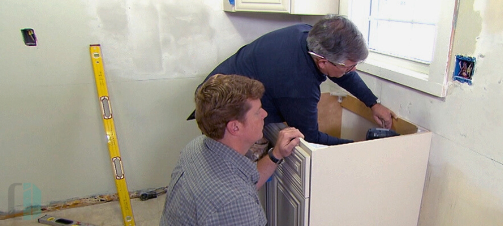 Two people installing base cabinets in a kitchen